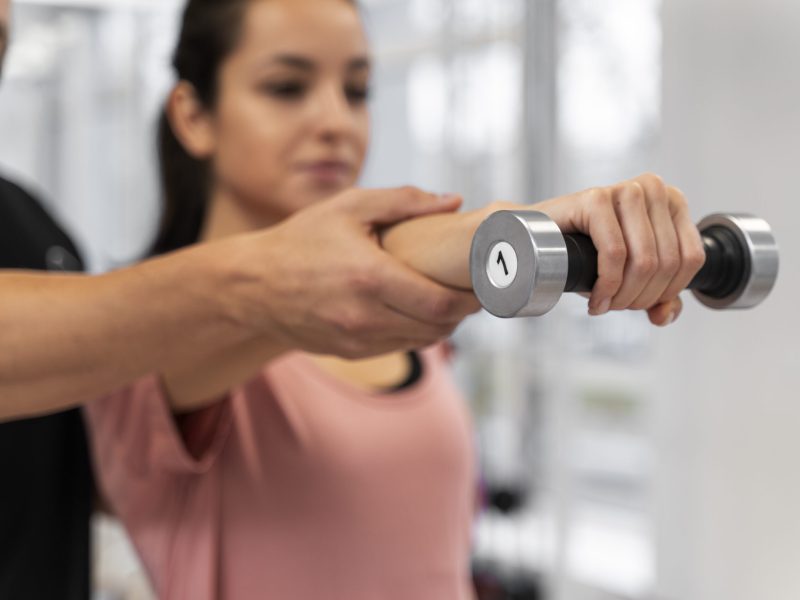Femme guidée par un coach pour un exercice avec un haltère d’un kilo