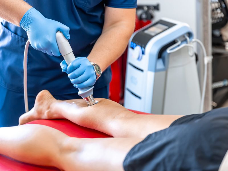 Traitement du tibia avec un appareil à ondes de choc par un professionnel de santé portant des gants